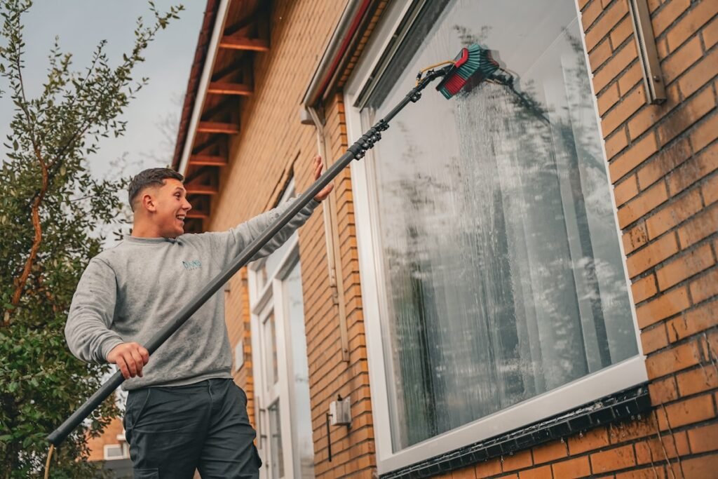 Tradesperson holding a long-reach gutter cleaning pole in front of a house
