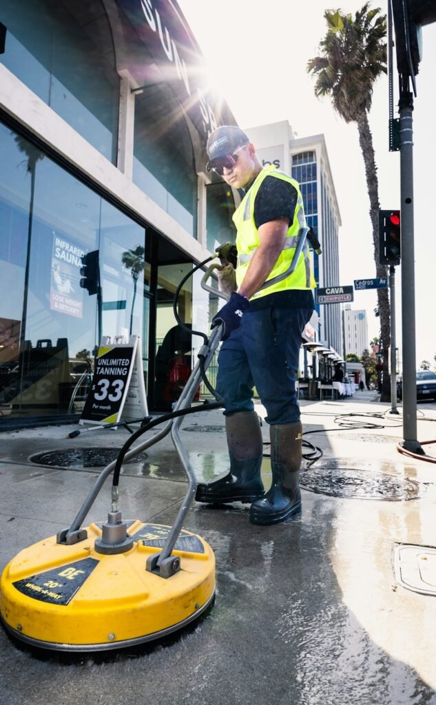 Operative in high-visibility workwear pressure washing an outdoor surface